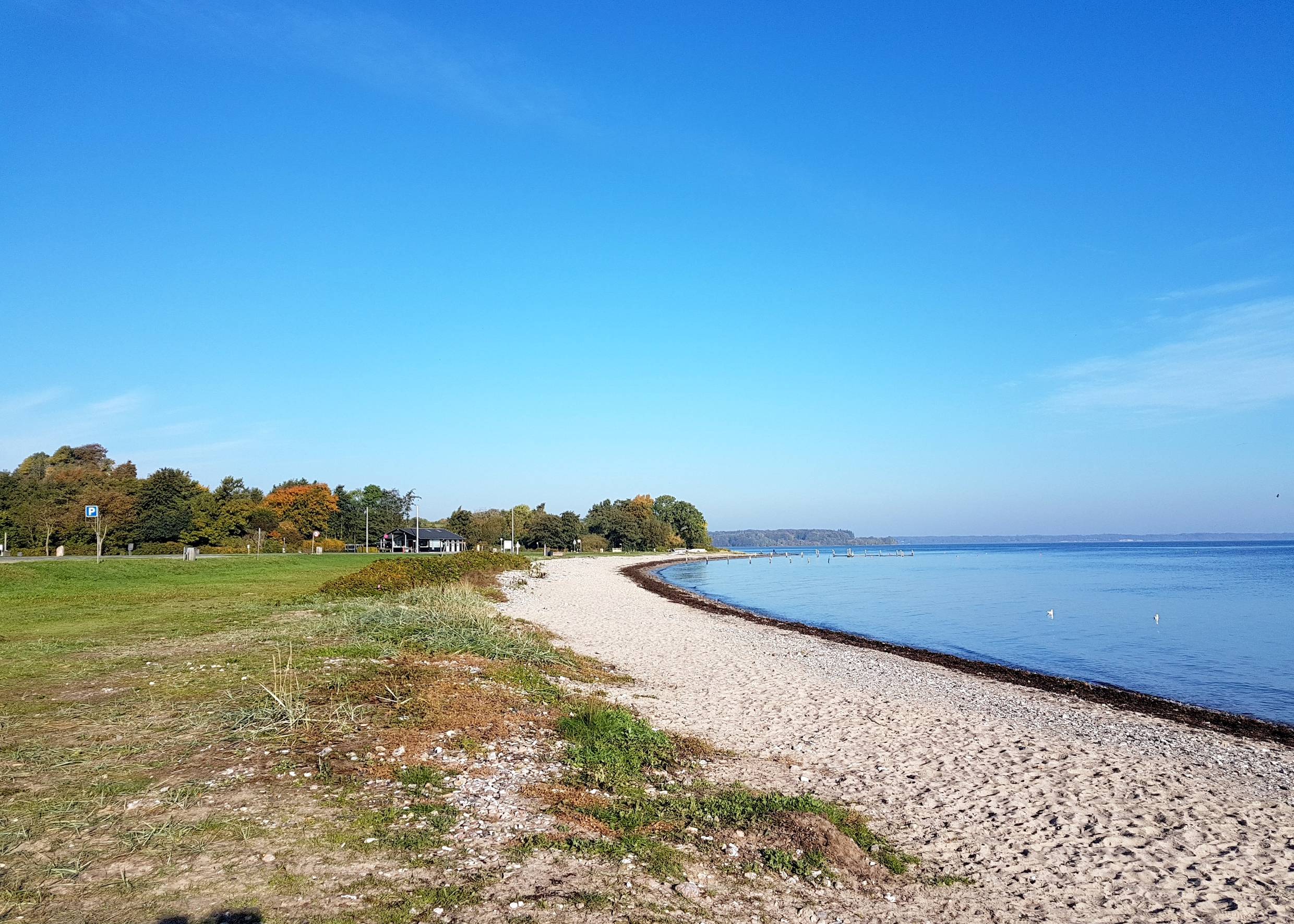 Schmaler Strand mit einer Wiese, sehr stilles blaues Meer 