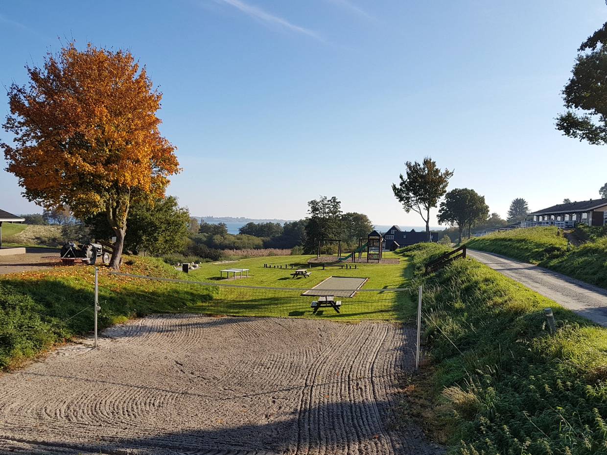 Ein Beachvolleyballfeld, dahinter Spielgeräte auf einer Wiese am Hang