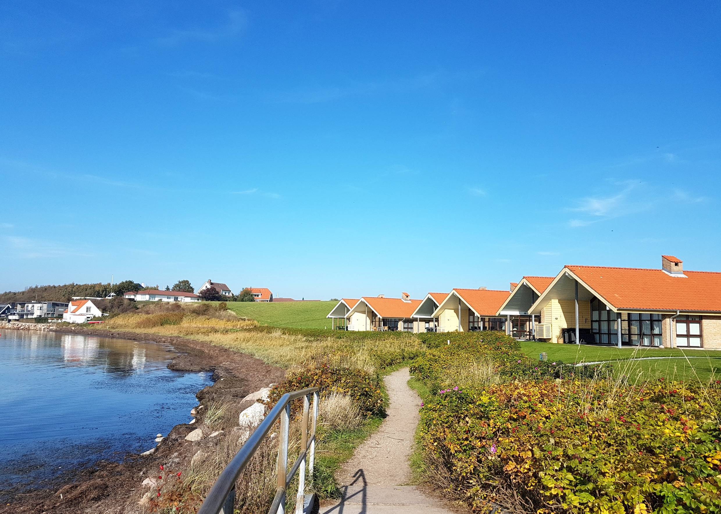verschiedene Ferienhäuser an der Küste, davor ein Wanderweg