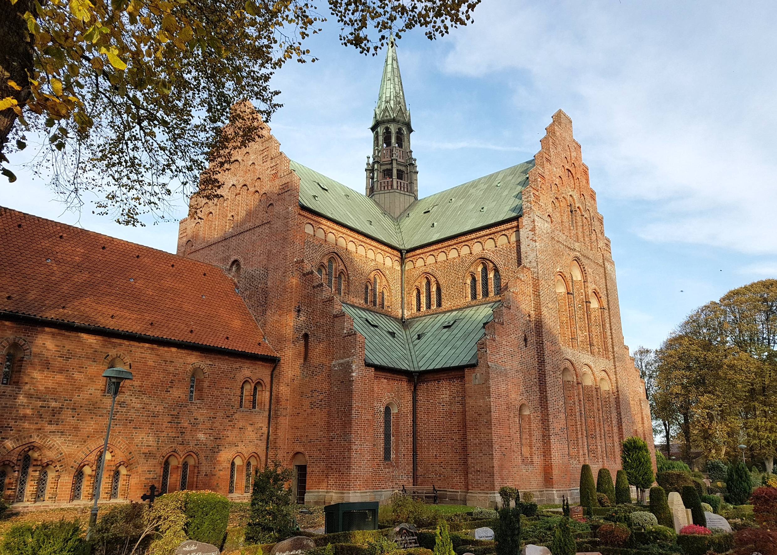 Große Backsteimkirche mit Kupeferdach, davor ein Friedhof