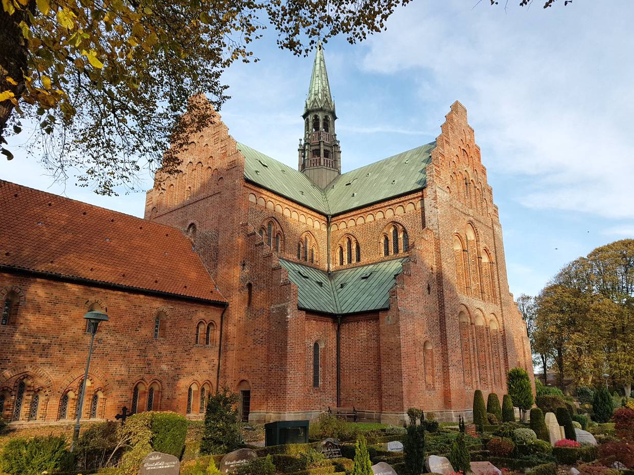 Große Backsteimkirche mit Kupeferdach, davor ein Friedhof