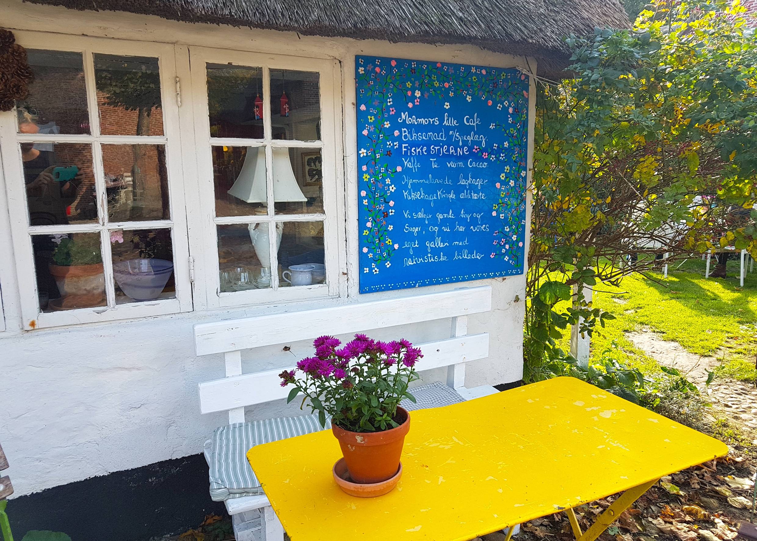 Gelber Tisch mit Blumen vor einem weißen Reetdachhaus