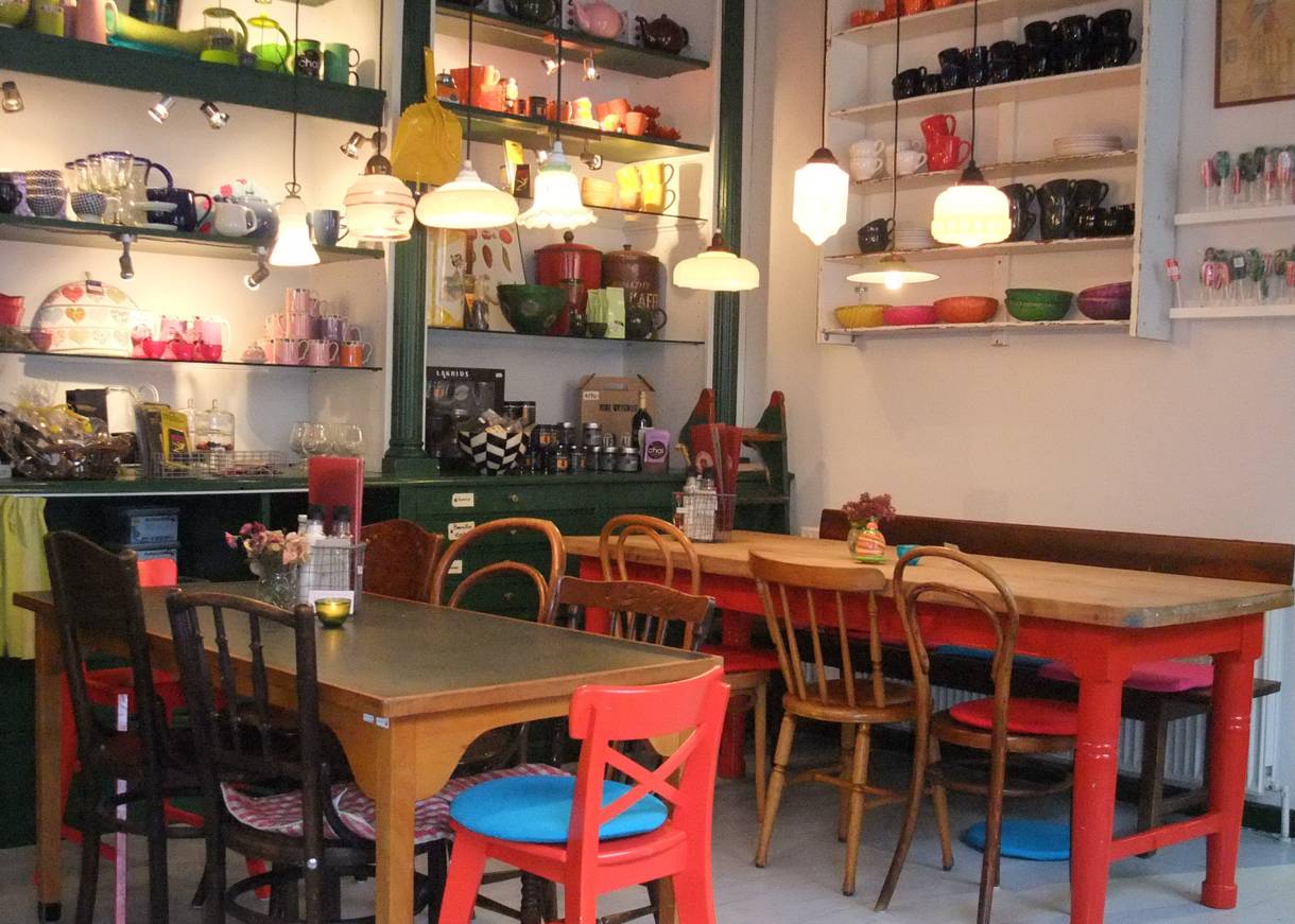 Buntes Café-Mobiliar, dahinter Regale mit Geschirr