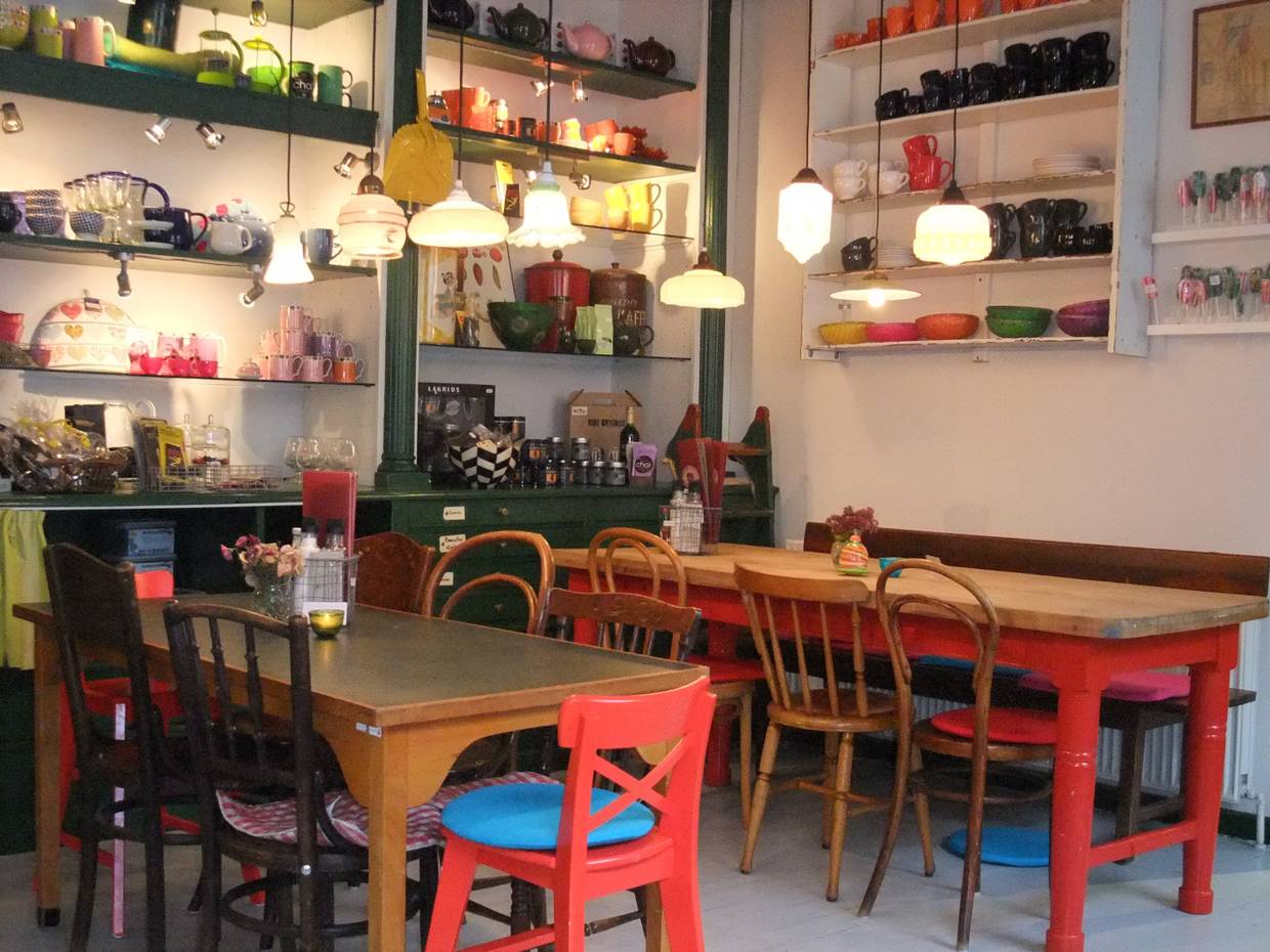 Buntes Café-Mobiliar, dahinter Regale mit Geschirr