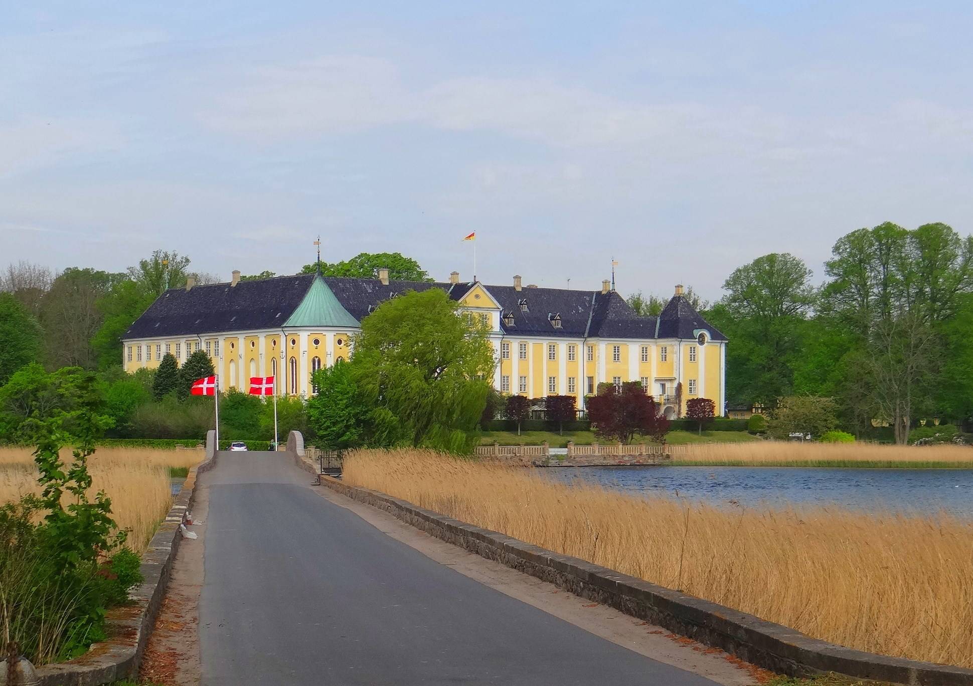 Eine schmale, aspfaltierte Straße in Richtung eines großen und gelben Schlosses