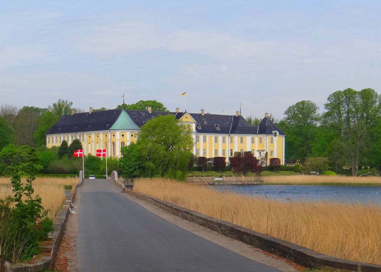 Eine schmale, aspfaltierte Straße in Richtung eines großen und gelben Schlosses