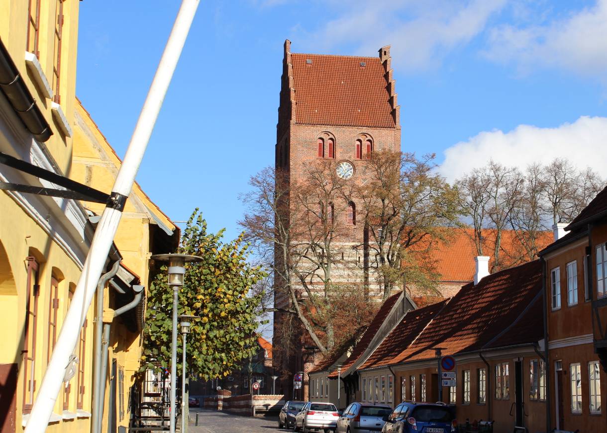 Gasse mit alten Häusern und einem großen Kirchturm aus Backstein im Hintergrund