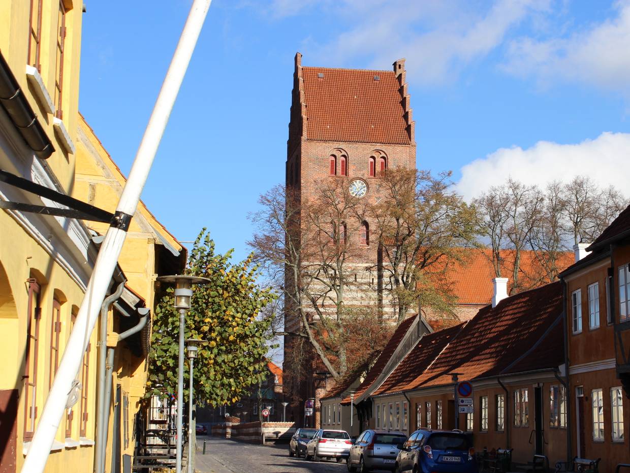 Gasse mit alten Häusern und einem großen Kirchturm aus Backstein im Hintergrund