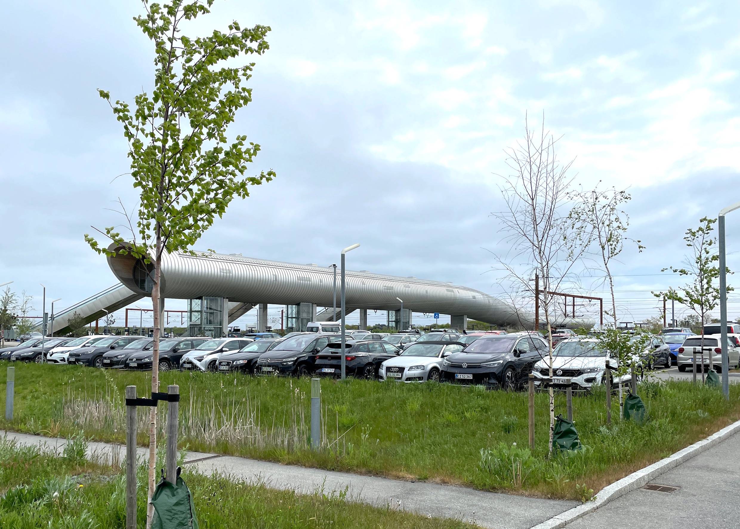 Blick über eine Parkplatz auf eine moderne Fußgängerbrücke am Bahnhof