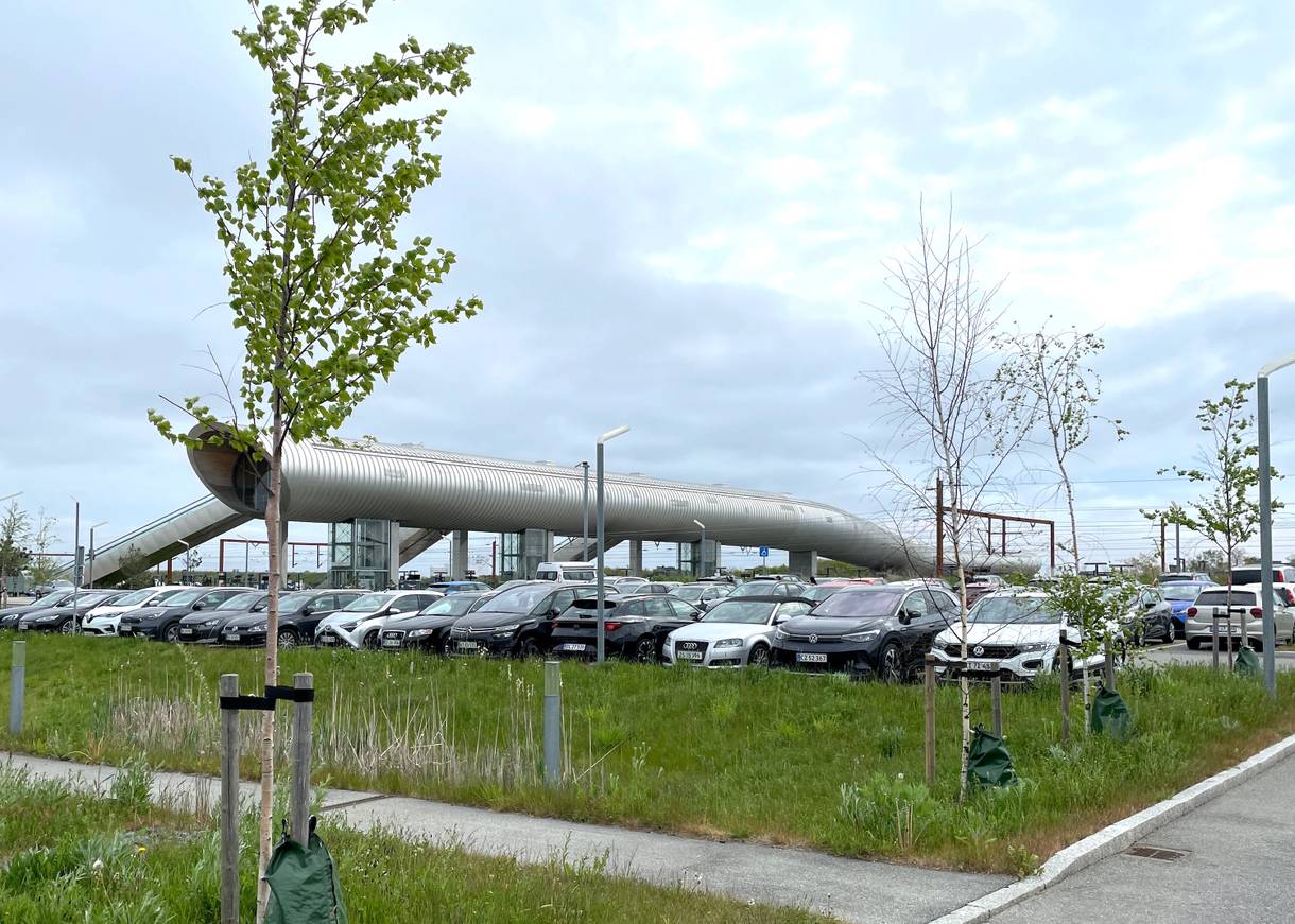 Blick über eine Parkplatz auf eine moderne Fußgängerbrücke am Bahnhof