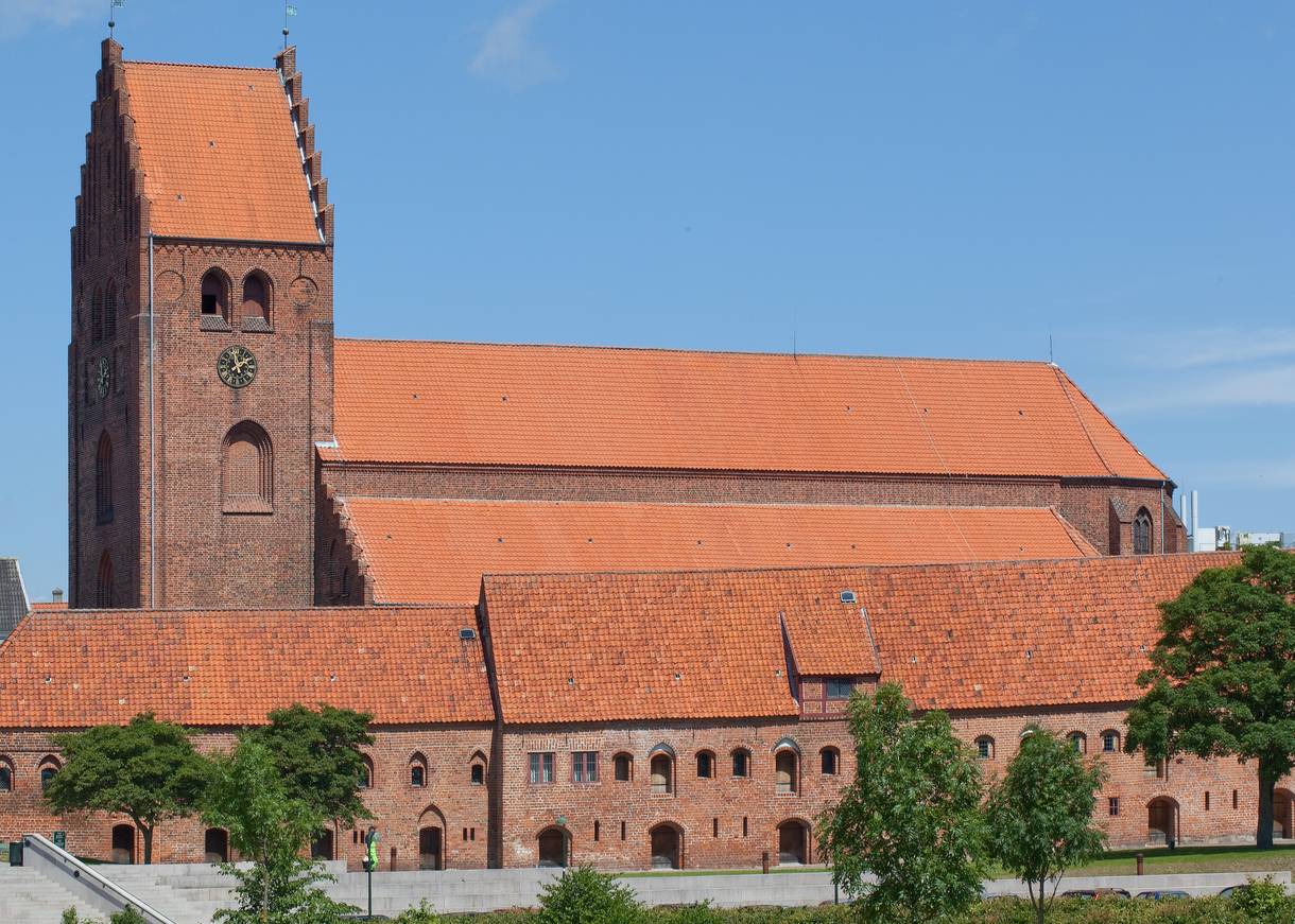 Große, rote Backsteinkirche mit historischen Gebäuden davor