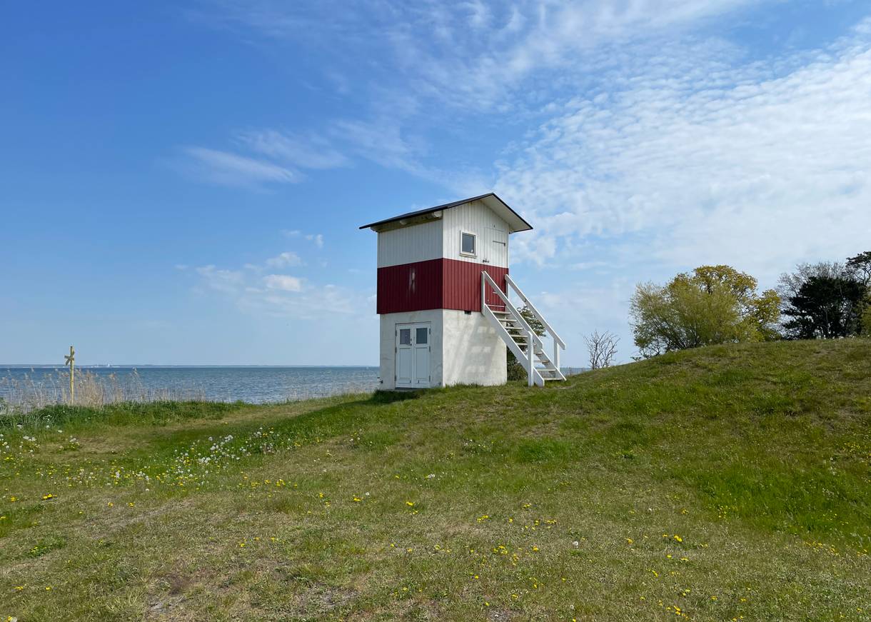 Rot-weißer Holztturm auf einer Wiese am Meer