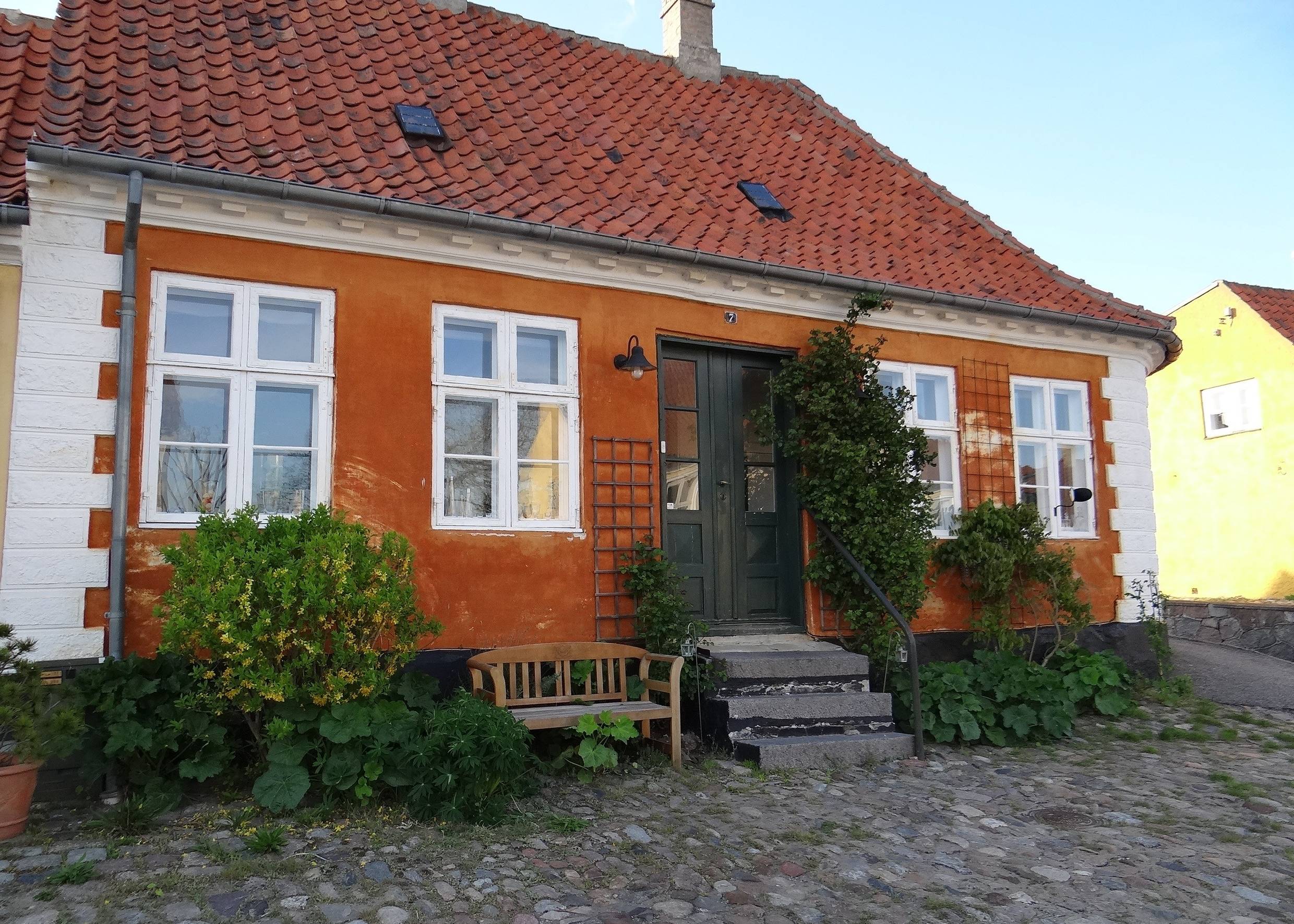 Altes, orangenes Haus mit einer kleinen Holzbank und Kopfsteinpflaster davor