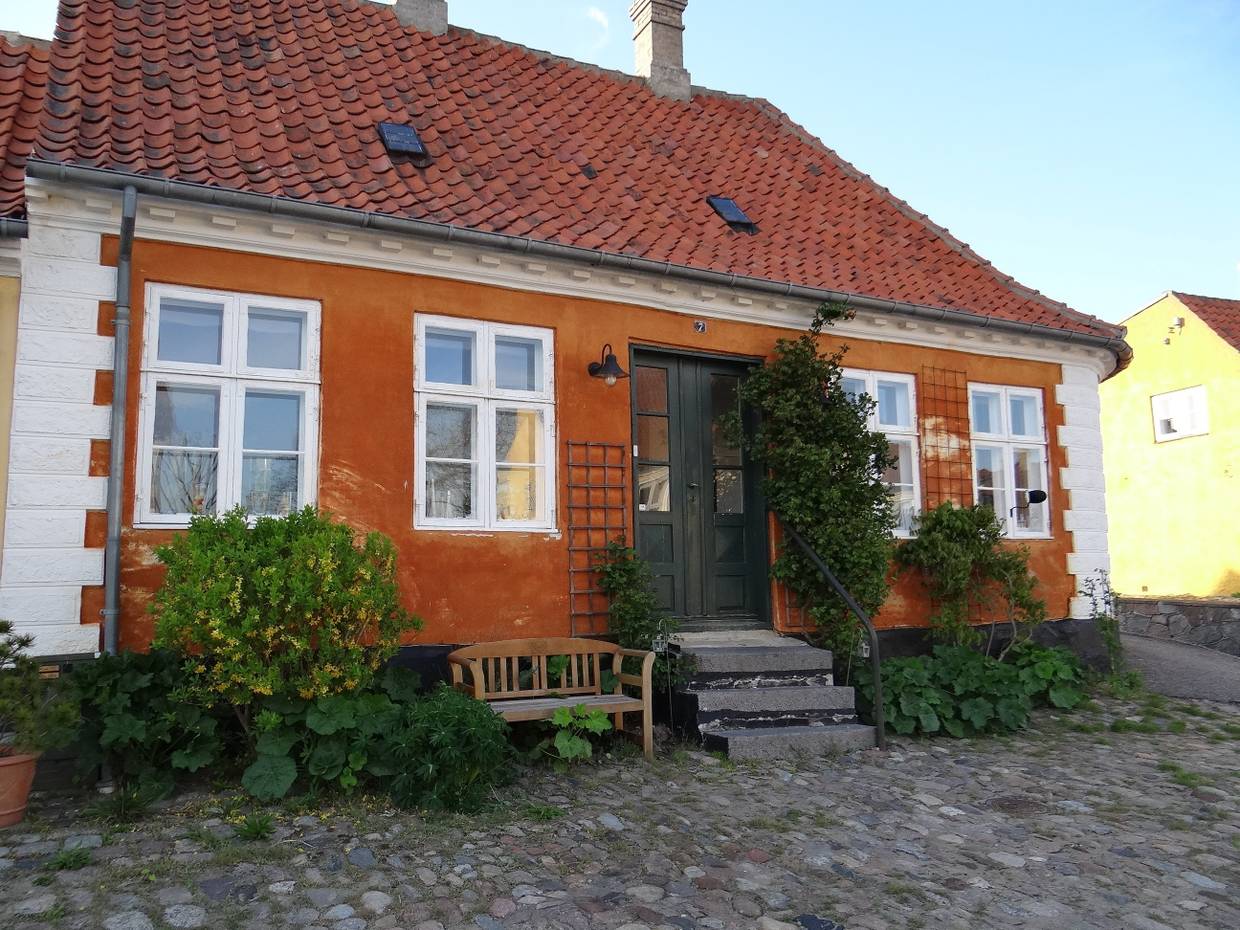 Altes, orangenes Haus mit einer kleinen Holzbank und Kopfsteinpflaster davor