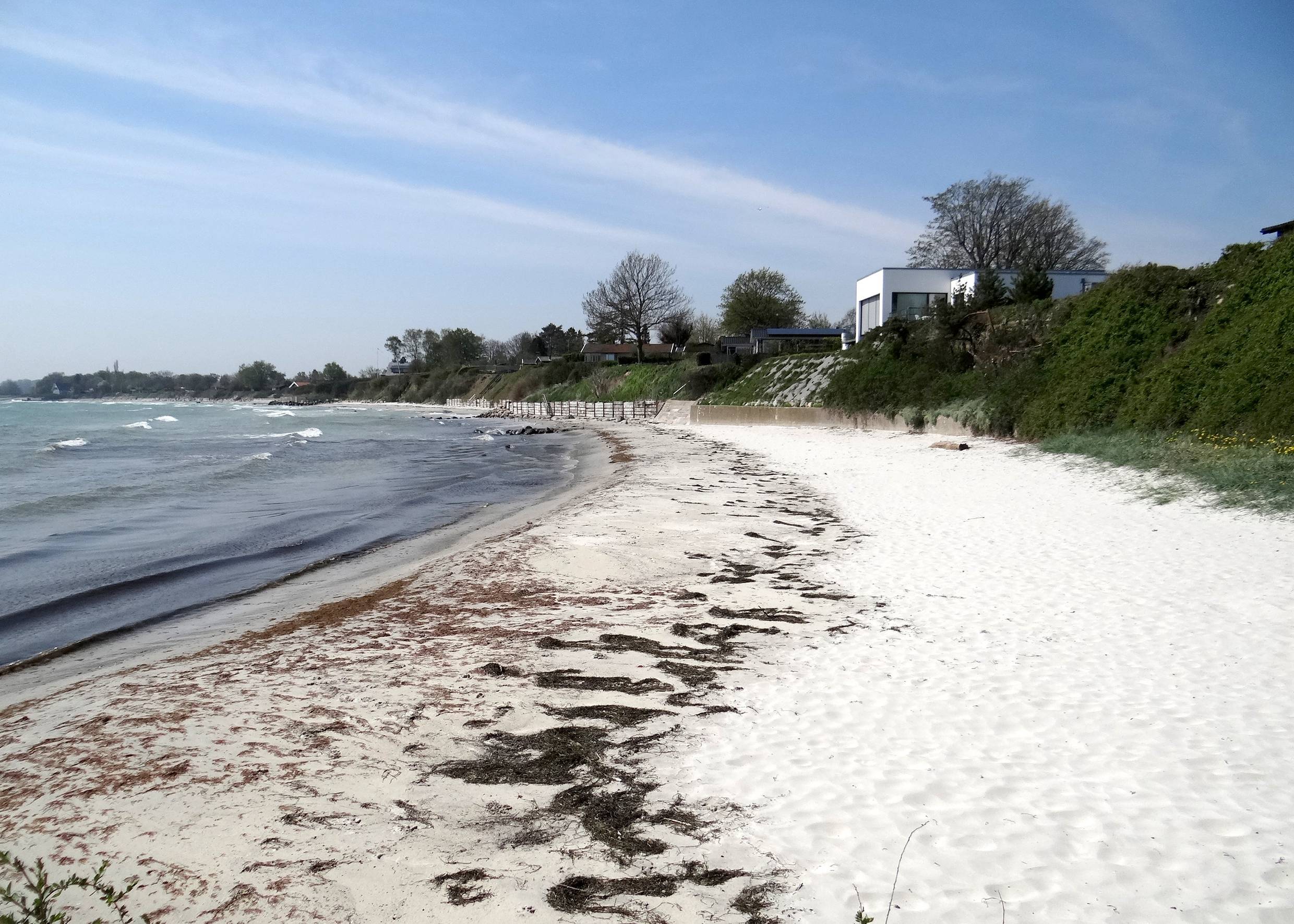 Kleiner, weißer Sandstrand unter einem grünen Hang