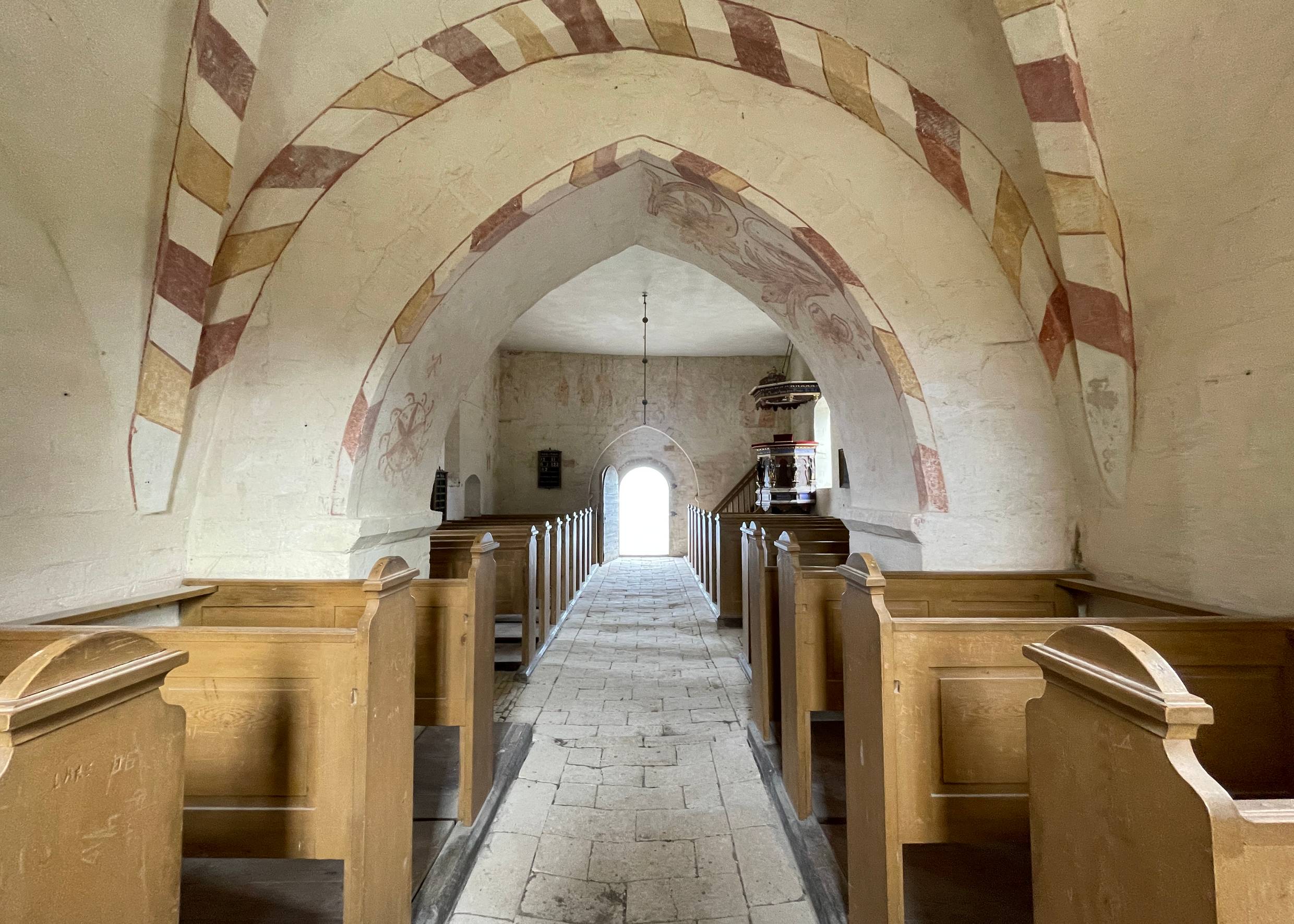 Blick durch ein altes Kirchenschiff mit Holzbänken und bemalten Kalkwänden
