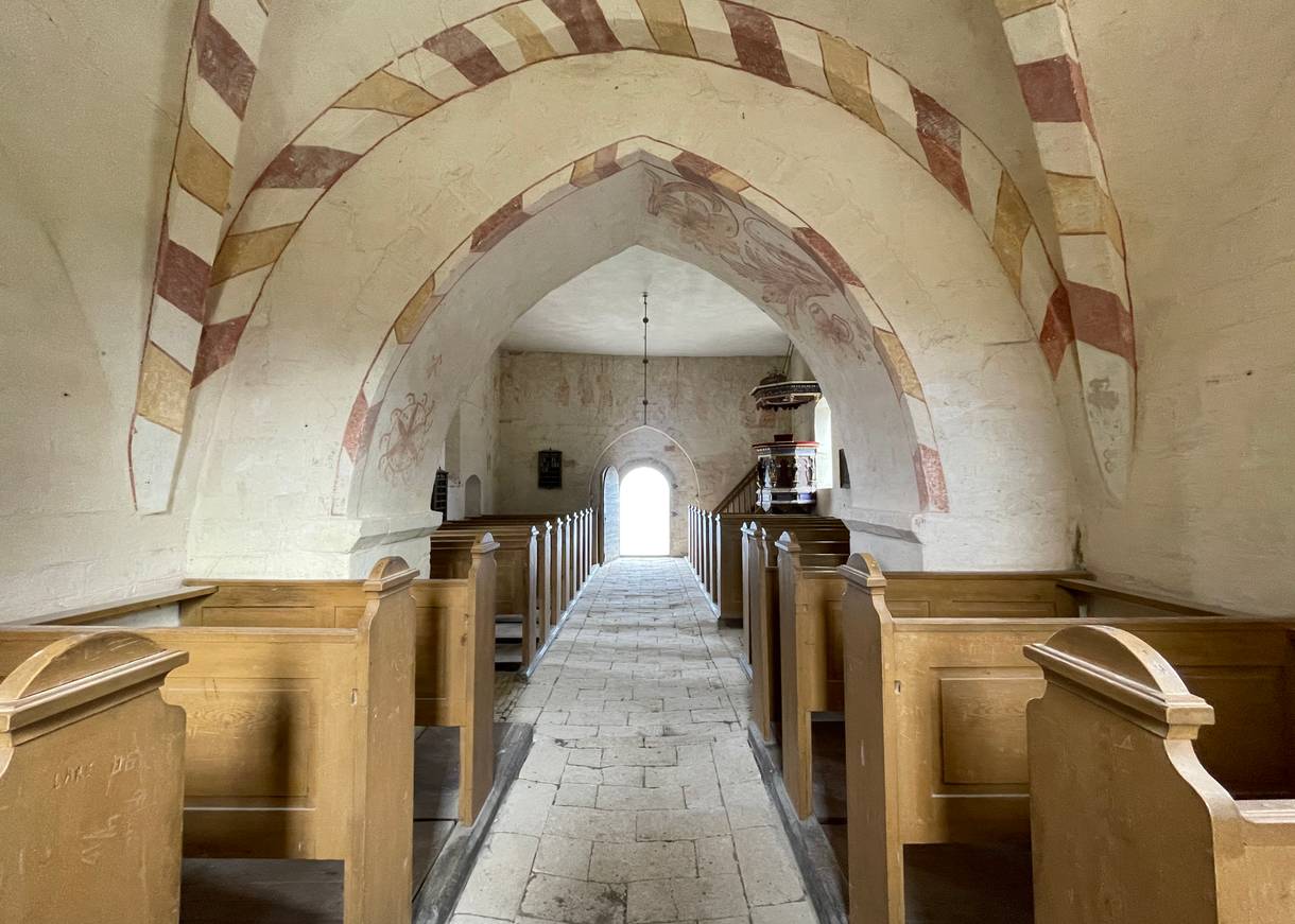 Blick durch ein altes Kirchenschiff mit Holzbänken und bemalten Kalkwänden
