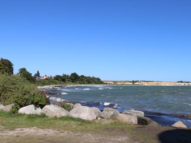 Bucht mit viel Grün, ein schmaler Sandstrand und Ferienhäuser, im Hintergrund ein kreidefelsen