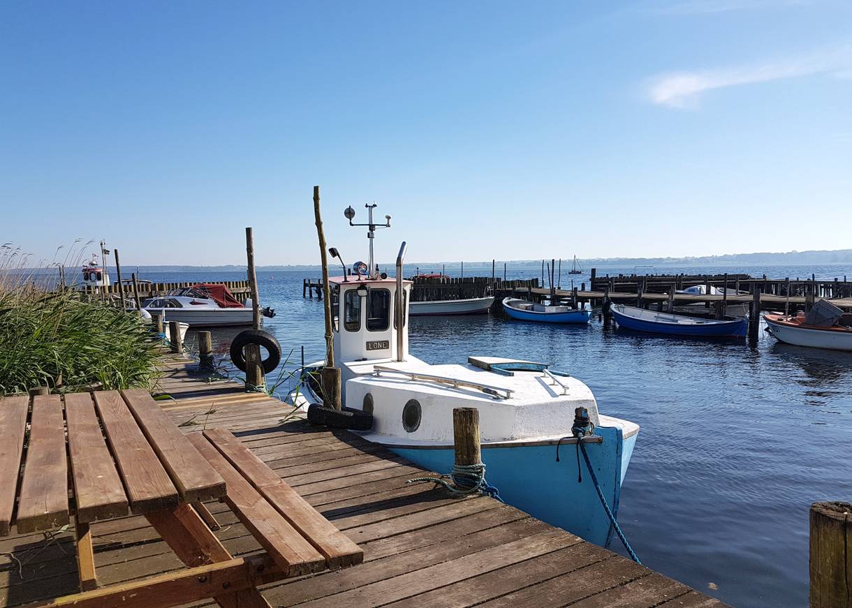 Blauweißes Holzboot an einem Holzsteg in einer schmalen Hafenbucht