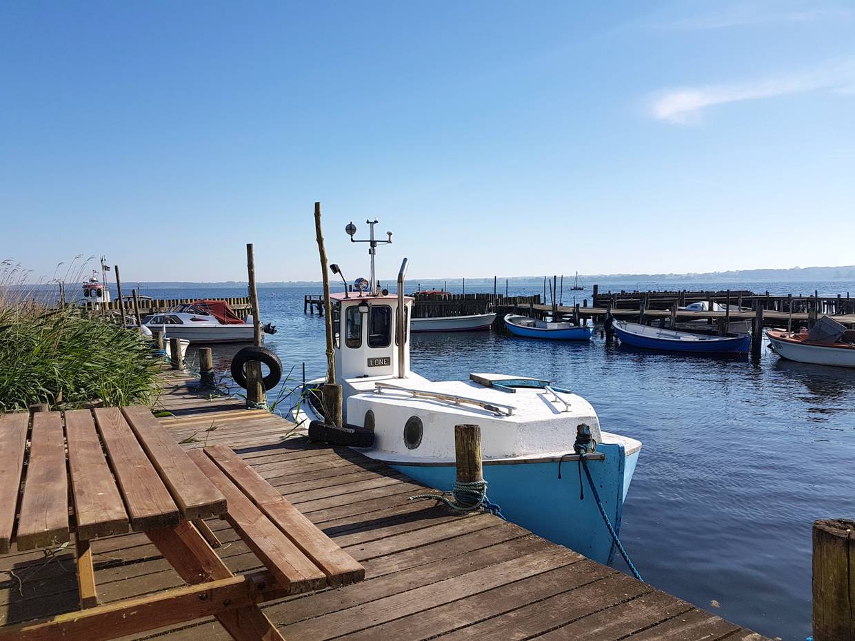 Blauweißes Holzboot an einem Holzsteg in einer schmalen Hafenbucht