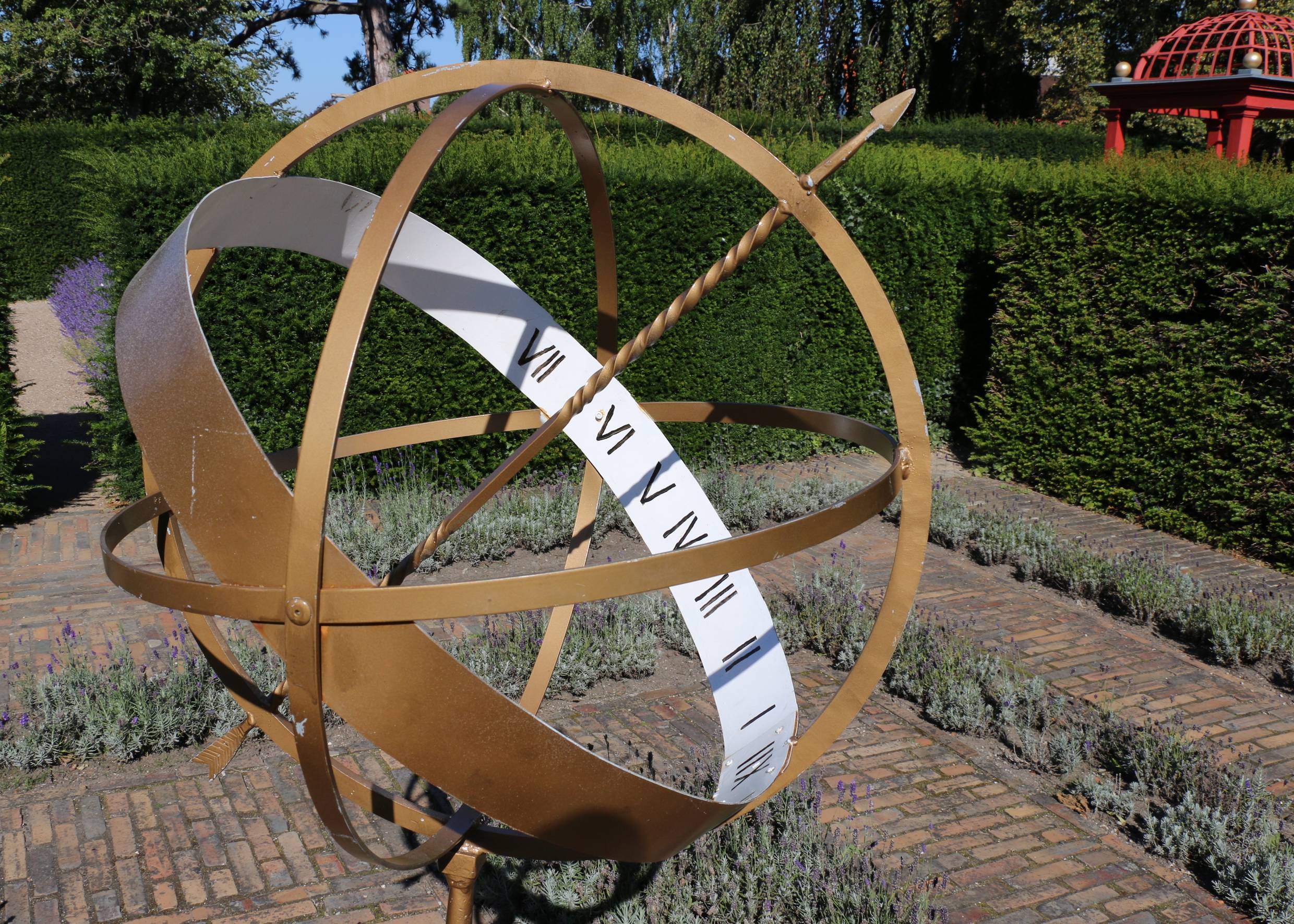 Sonnenuhr aus Kupfer vor einer grünen Hecke