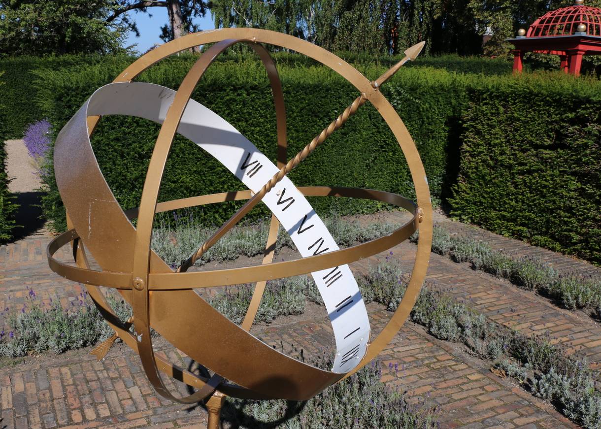 Sonnenuhr aus Kupfer vor einer grünen Hecke
