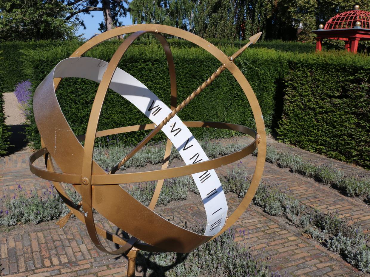 Sonnenuhr aus Kupfer vor einer grünen Hecke