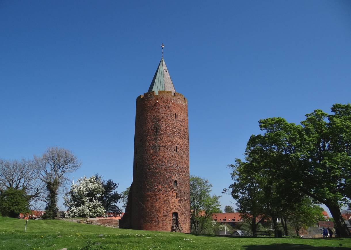 Ein mächtiger, runder Backsteinturm mit einer goldenen Gans auf dem Dach 
