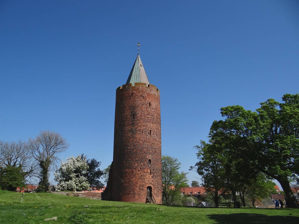 Ein mächtiger, runder Backsteinturm mit einer goldenen Gans auf dem Dach 