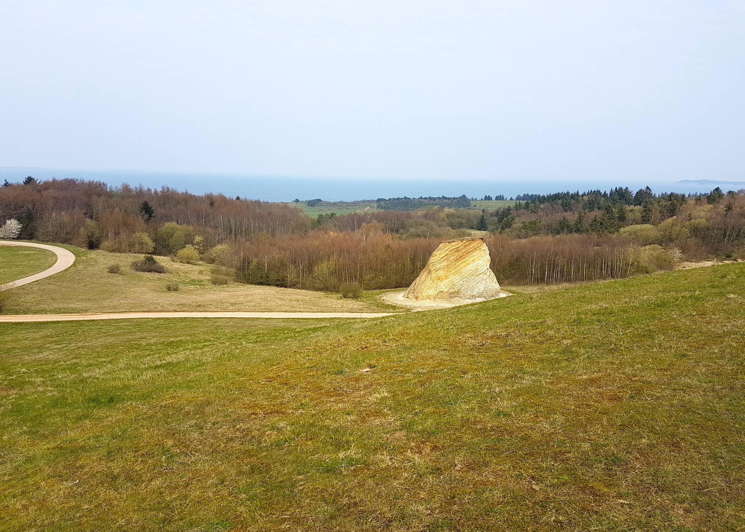 Blick von einem Hügel auf einen tiefer gelegenen, rot-weiß gestreiften Felsen
