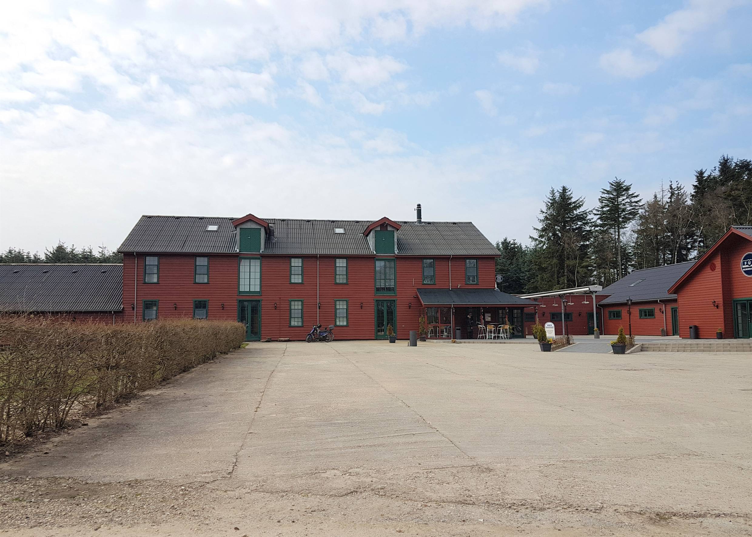 Rotes Holzhaus mit Nebengebäuden, davor ein leerer Platz