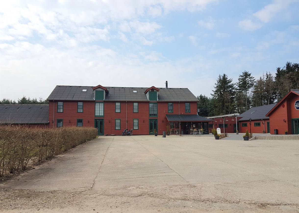 Rotes Holzhaus mit Nebengebäuden, davor ein leerer Platz