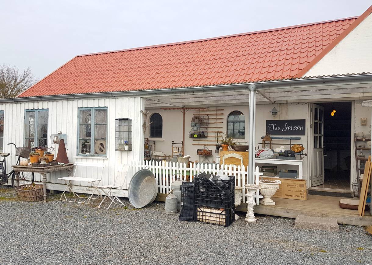 Veranda eines weißen Hauses mit einem Geschäft für Deko, davor eine Kiesfläche