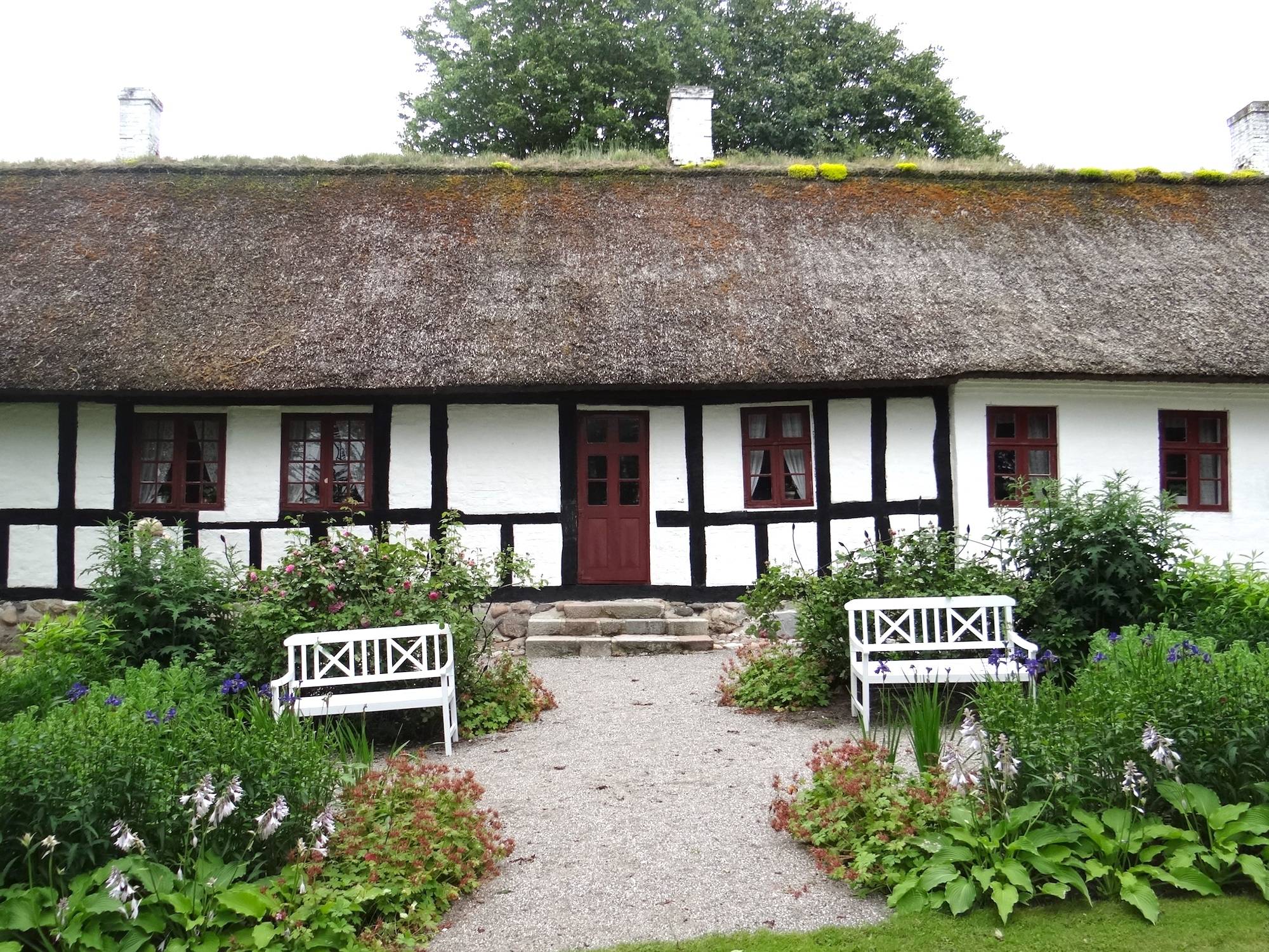 Weißes Fachwerkhaus, davor eine Bank und bunte Blumenbeete