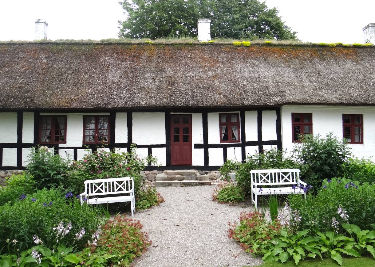 Weißes Fachwerkhaus, davor eine Bank und bunte Blumenbeete