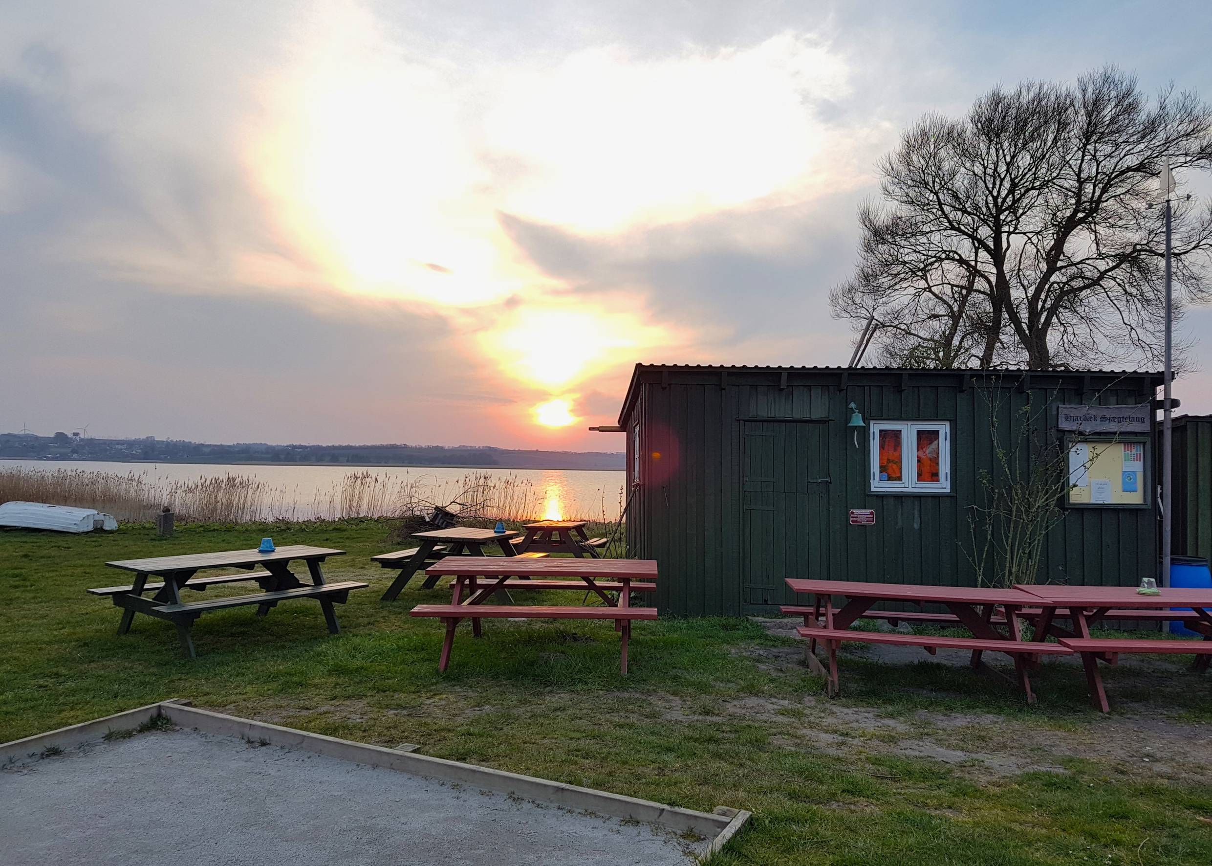 Sonnenuntergang hinter eine Fischerhütte und einem Baum, dahinter Wasser