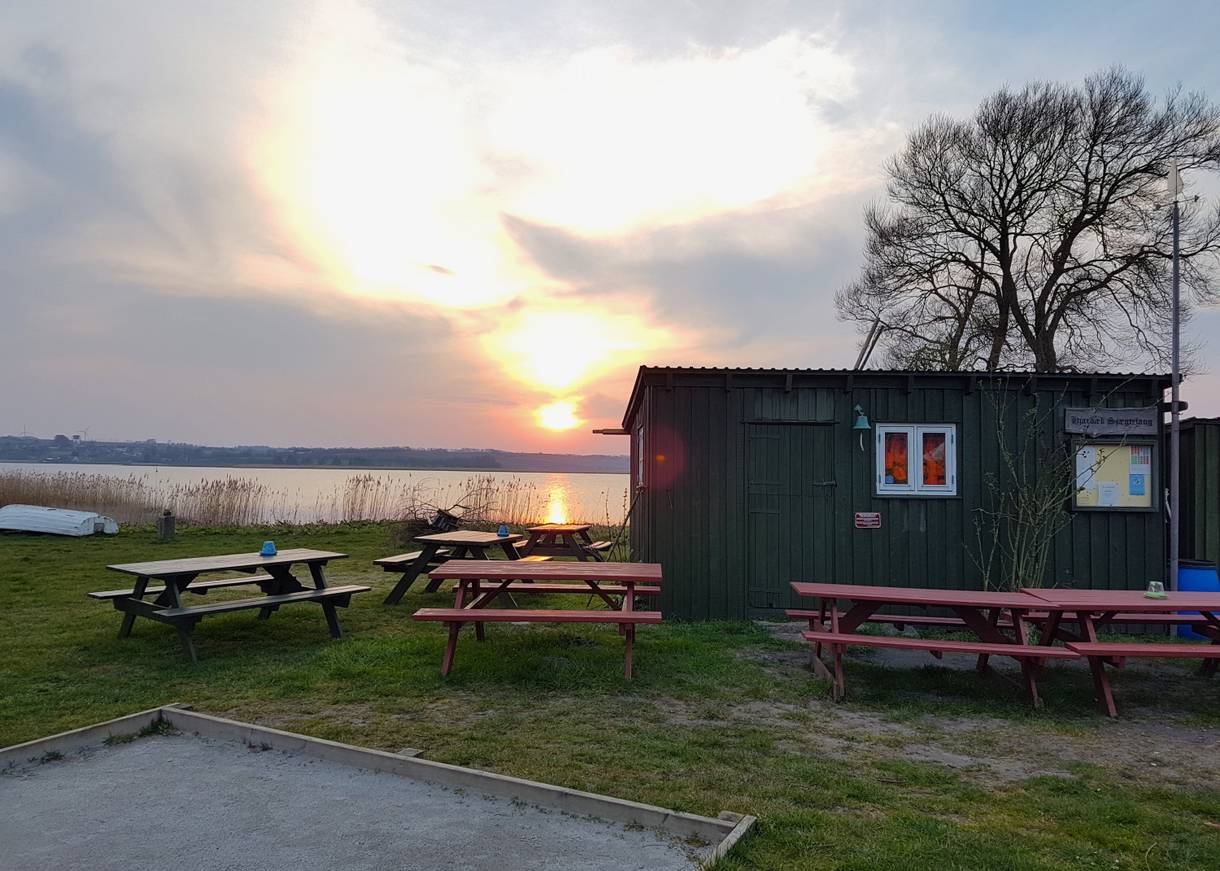 Sonnenuntergang hinter eine Fischerhütte und einem Baum, dahinter Wasser