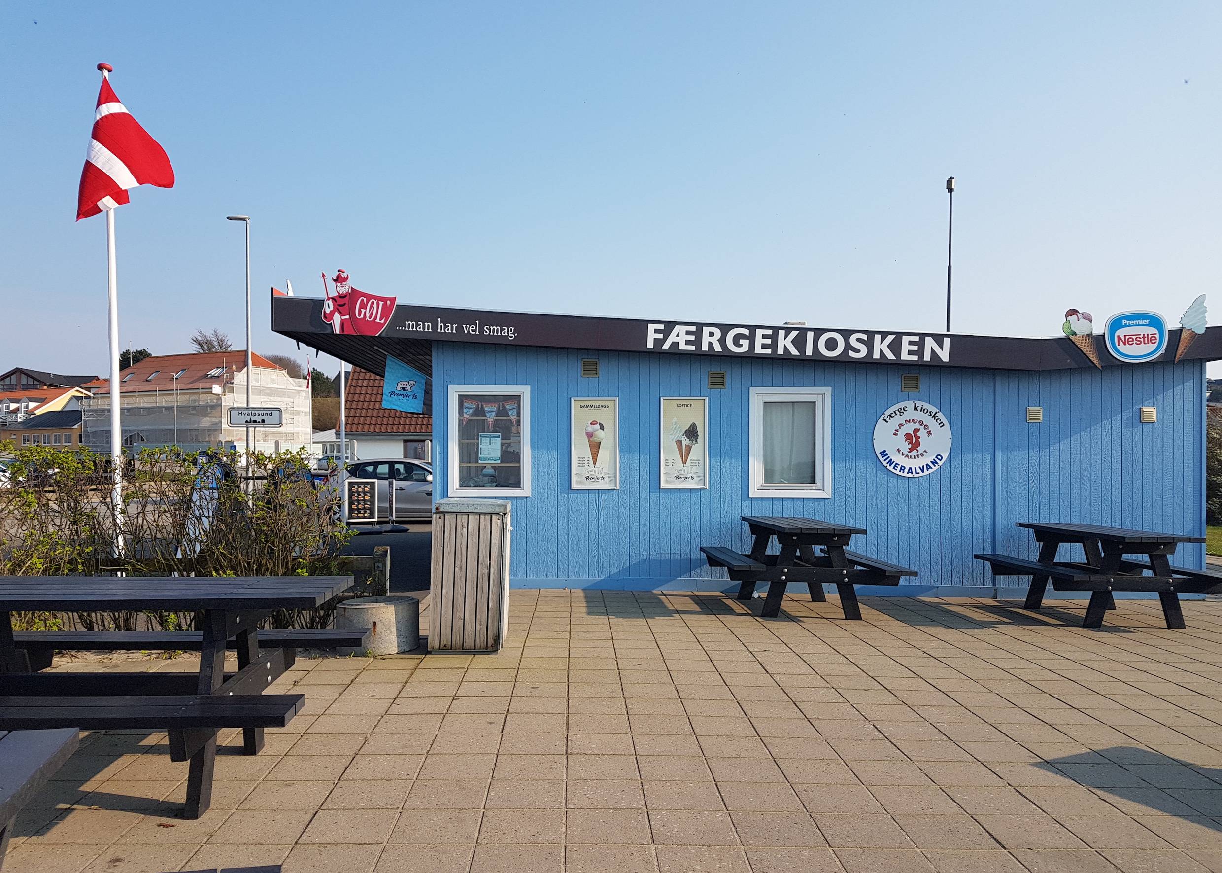 Hellblau gestrichener Hafenkiosk, davor eine dänische Fahne und Sitzplätze
