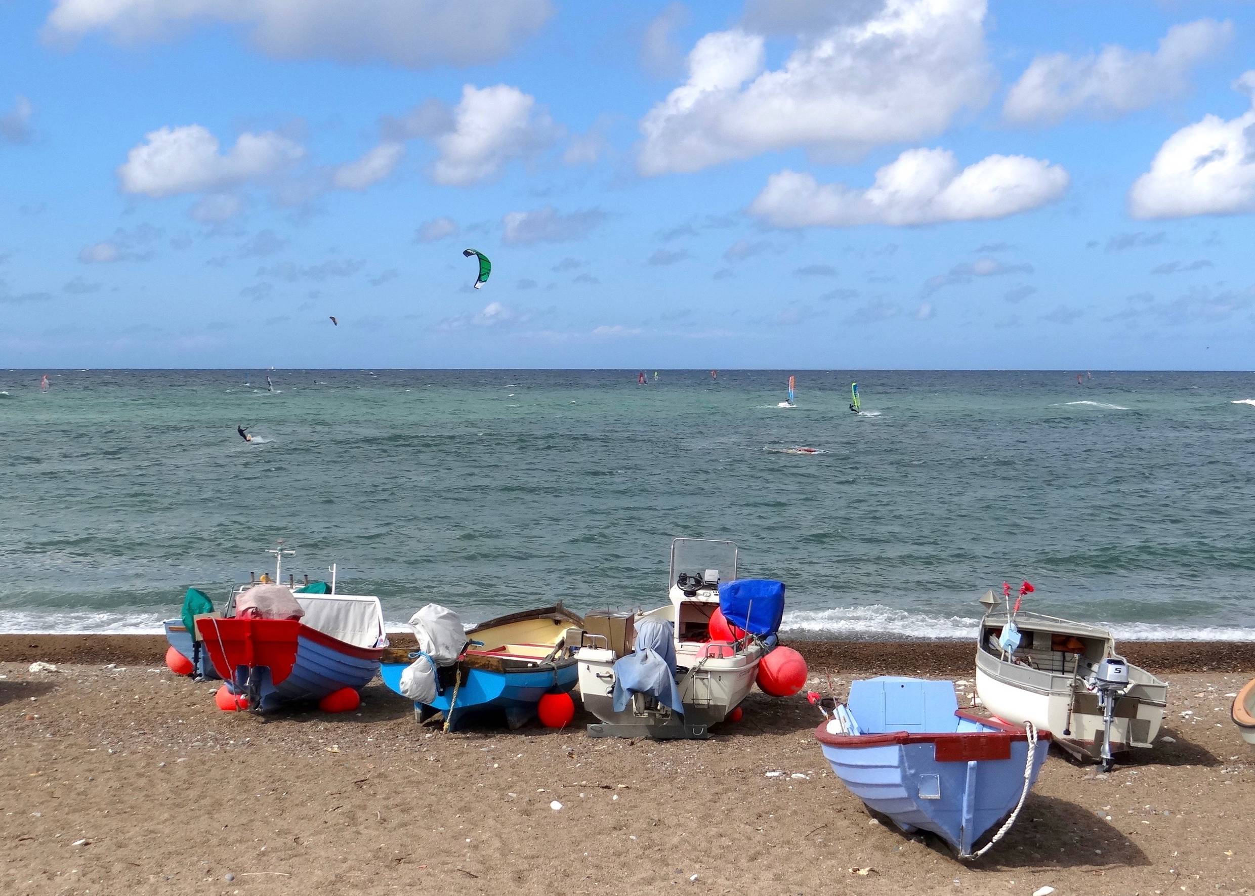 Kleine Fischerboote auf dem Strand, im Hintergrund die Surfer