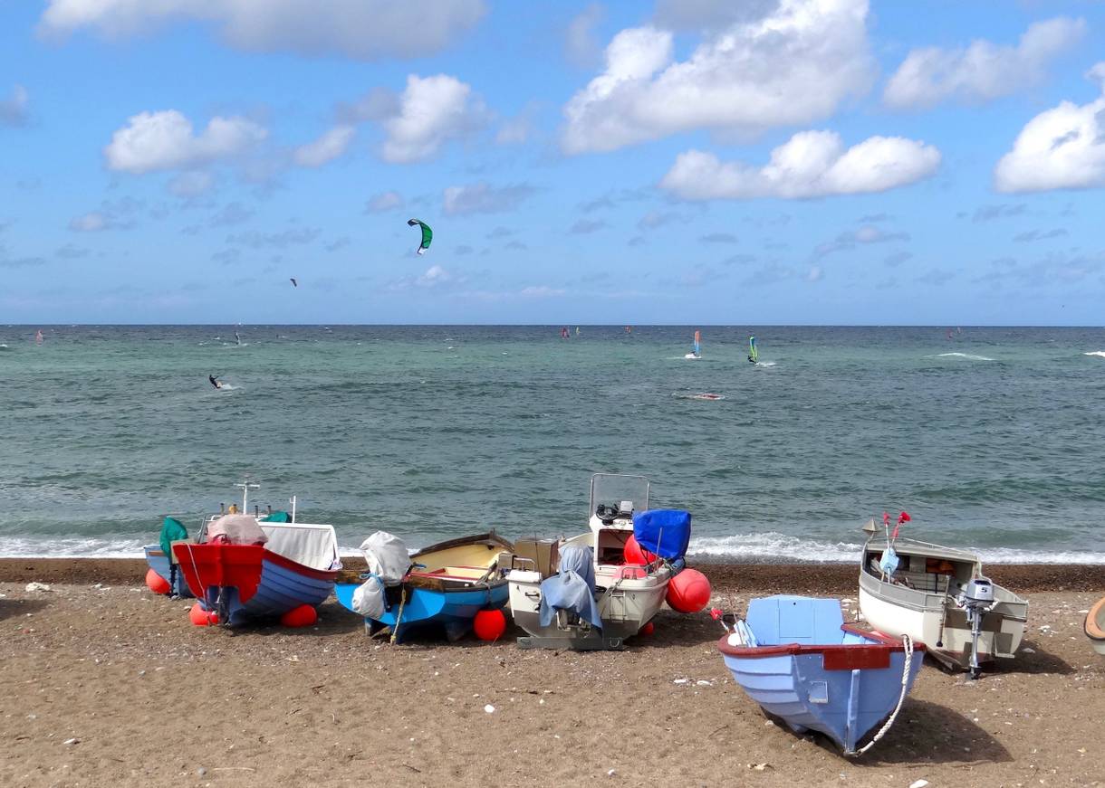 Kleine Fischerboote auf dem Strand, im Hintergrund die Surfer