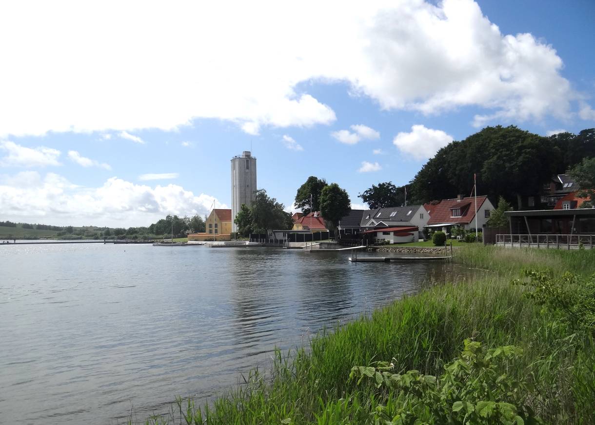 Blick über das Wasser auf Häuser und einen eckigen Turm am Fjordufer