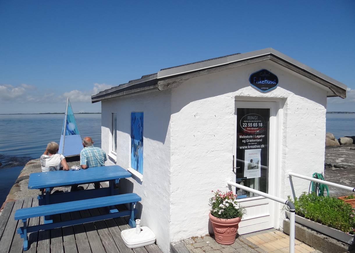 Weiße Steinhütte mit blauen Picknickbänken auf einer Holzterrasse am Wasser