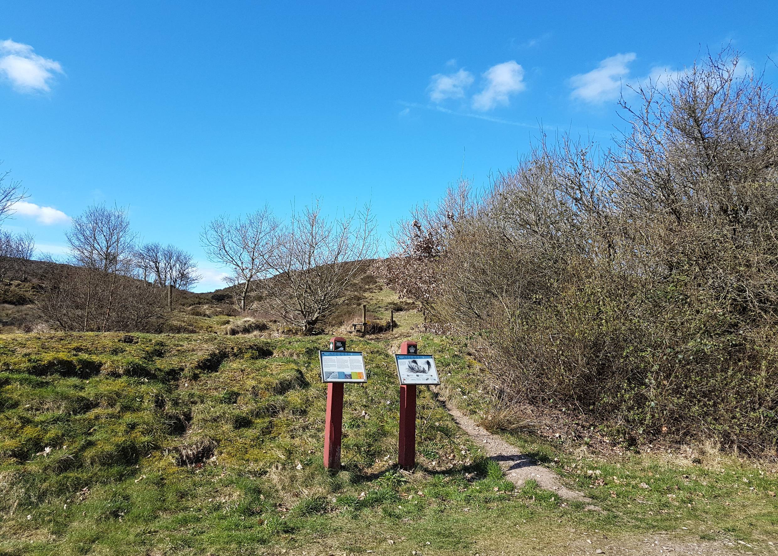 Schmaler Pfad durch die Landschaft, davor ein Hinweisschild