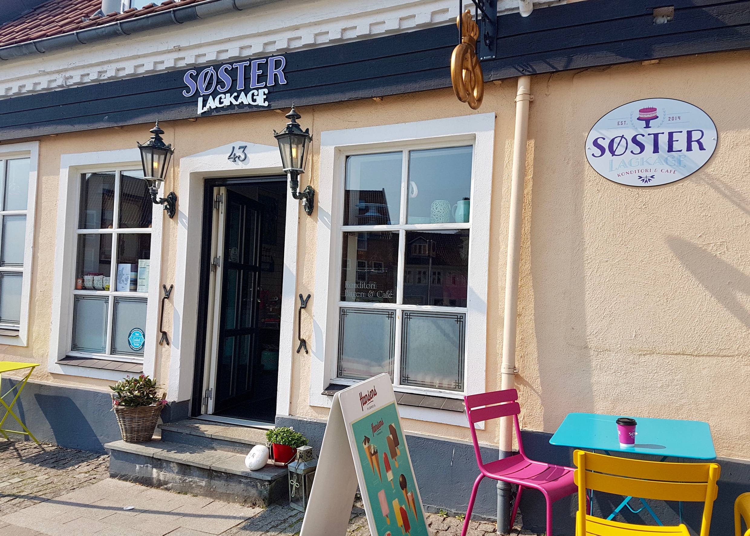 Weiße Sprossenfenster als Eingang zu einer kleinen Kaffeebar, davor bunte Tische