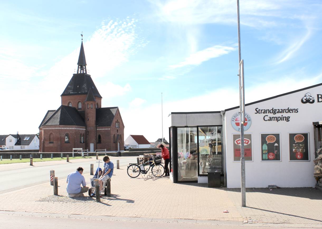 Supermarkt mit Passanten davor, dahinter eine Backsteinkirche