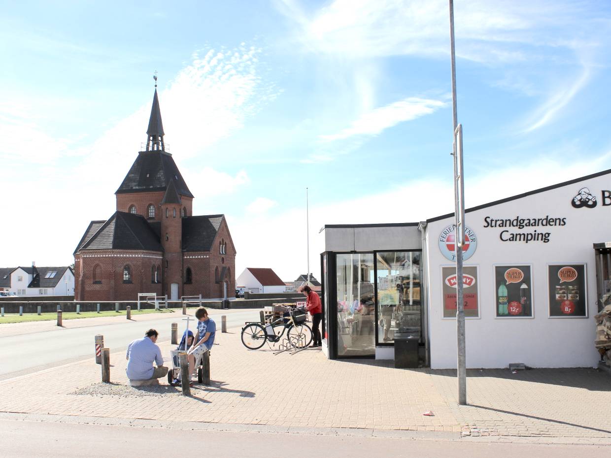 Supermarkt mit Passanten davor, dahinter eine Backsteinkirche
