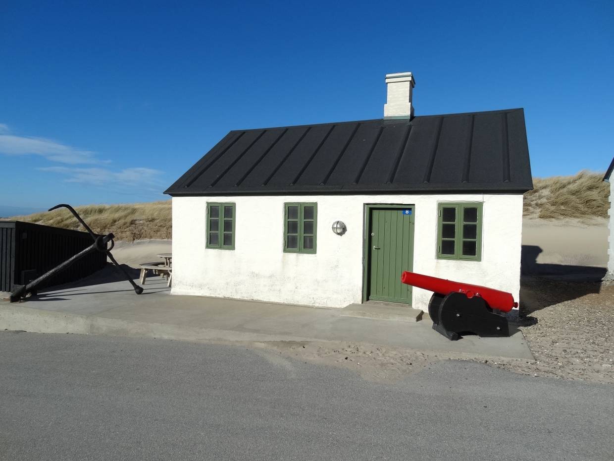 Kanone vor einer weißen Fischerhütte mit grüner Tür