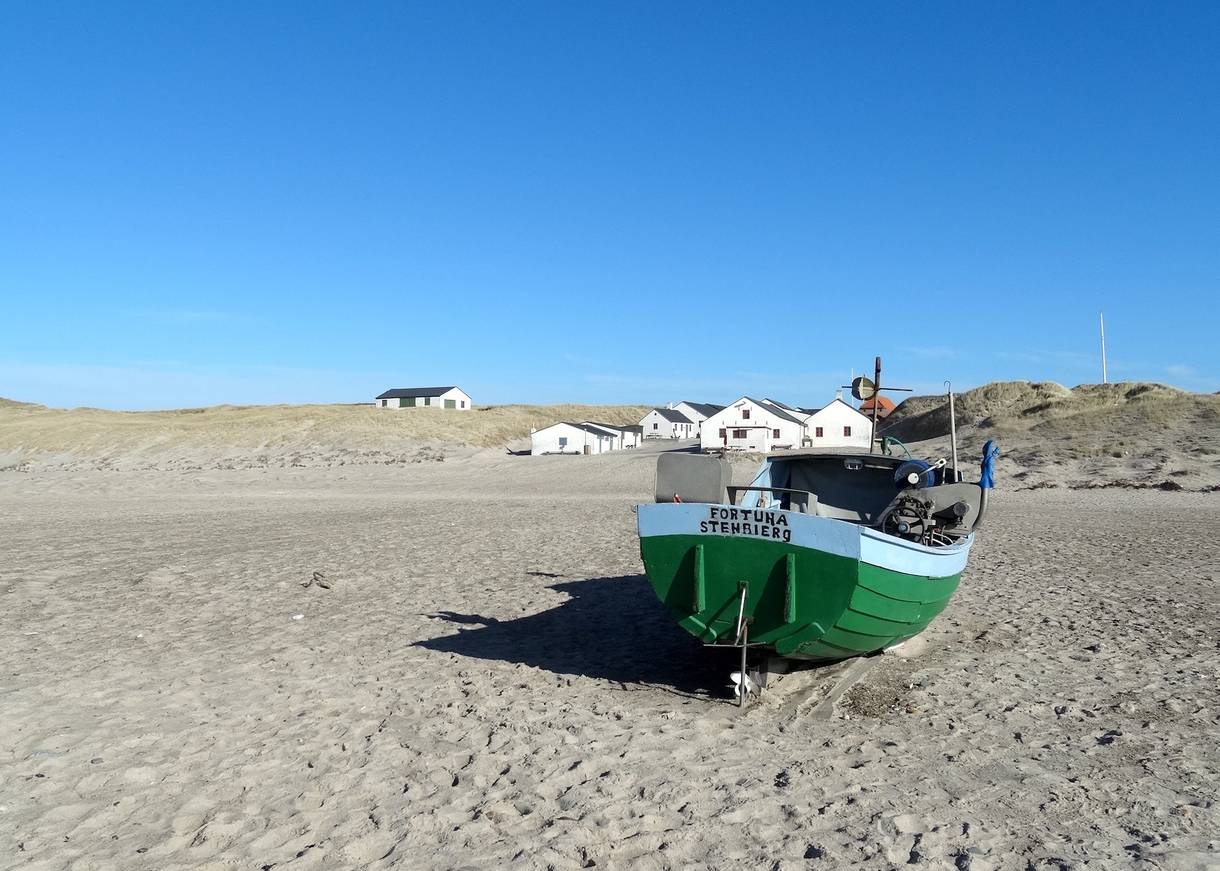 Grünes Fischerboot am Strand, dahinter die Fischerhütten