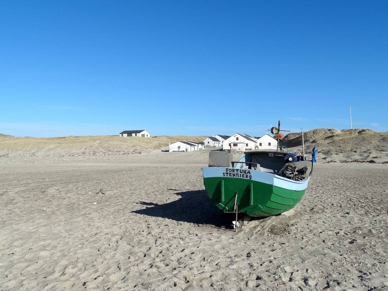 Grünes Fischerboot am Strand, dahinter die Fischerhütten