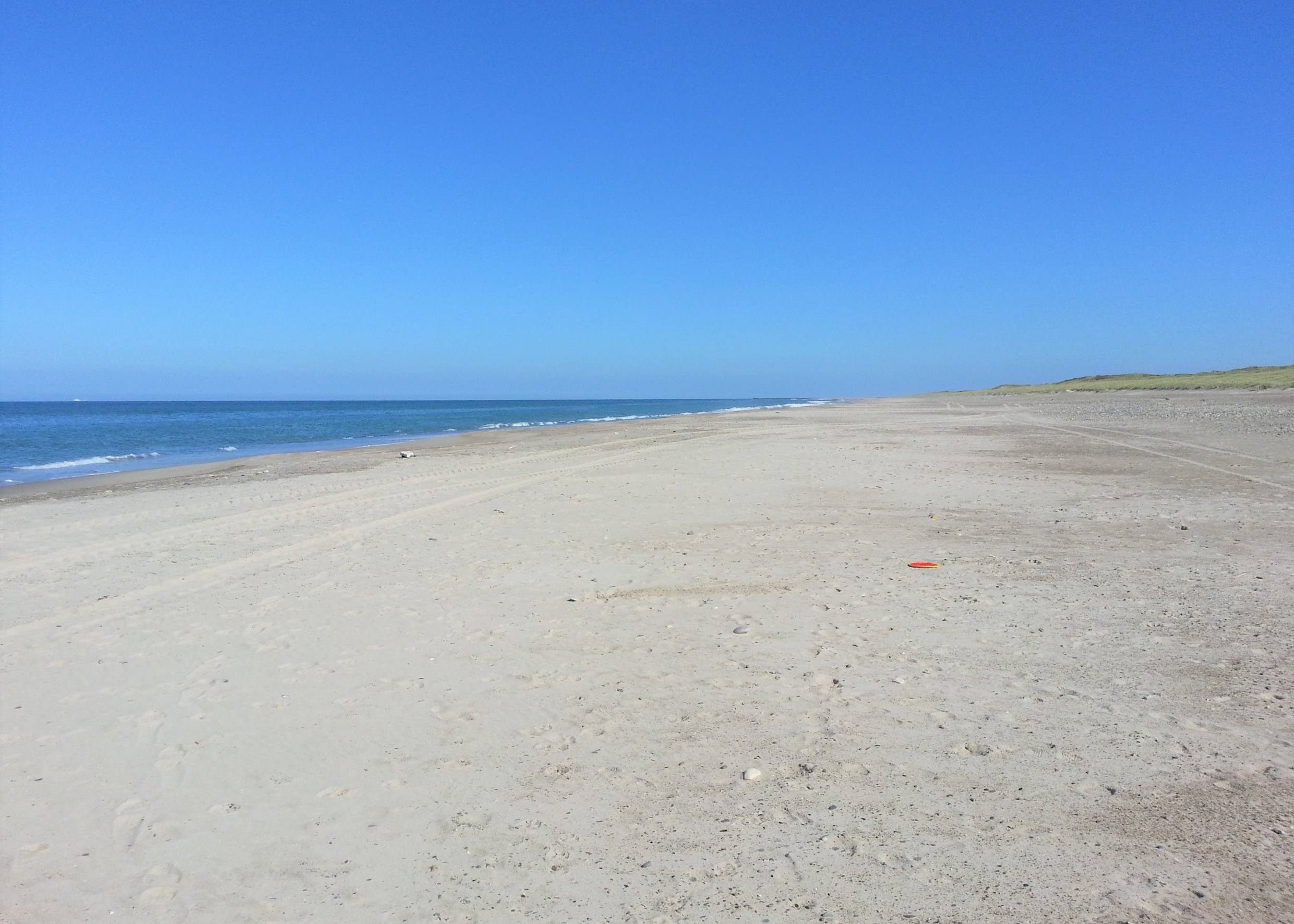 Sehr breiter, menschenleerer Strand unter blauem Himmel